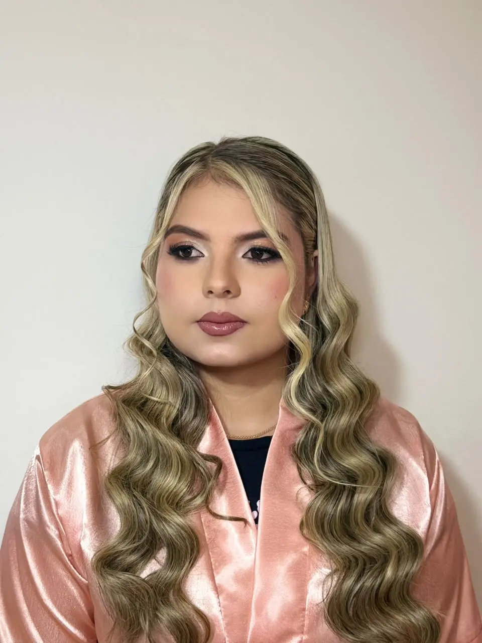Mujer posando algo de perfil con traje rosado un maquillaje social hecho por maquela, sentada.